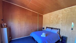 Ein modernes Schlafzimmer mit einer Wandpaneele aus Holz, einem Bett mit blauer Bettdecke und einem Nachttisch mit Lampe.