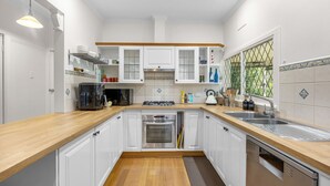 Una cocina moderna con armarios blancos, encimera de madera, electrodomésticos de acero inoxidable y vistas a la vegetación a través de una ventana.