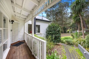 A covered porch with white railings, a wooden deck, and a view of a garden with various plants and trees. - Temple of the Hidden Grove – Tecoma Hills Sanctuary (Tecoma)