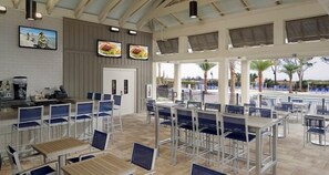 Un espace extérieur spacieux aménagé pour les repas, avec des tables et des chaises, un comptoir avec une machine à café et une vue sur la plage.