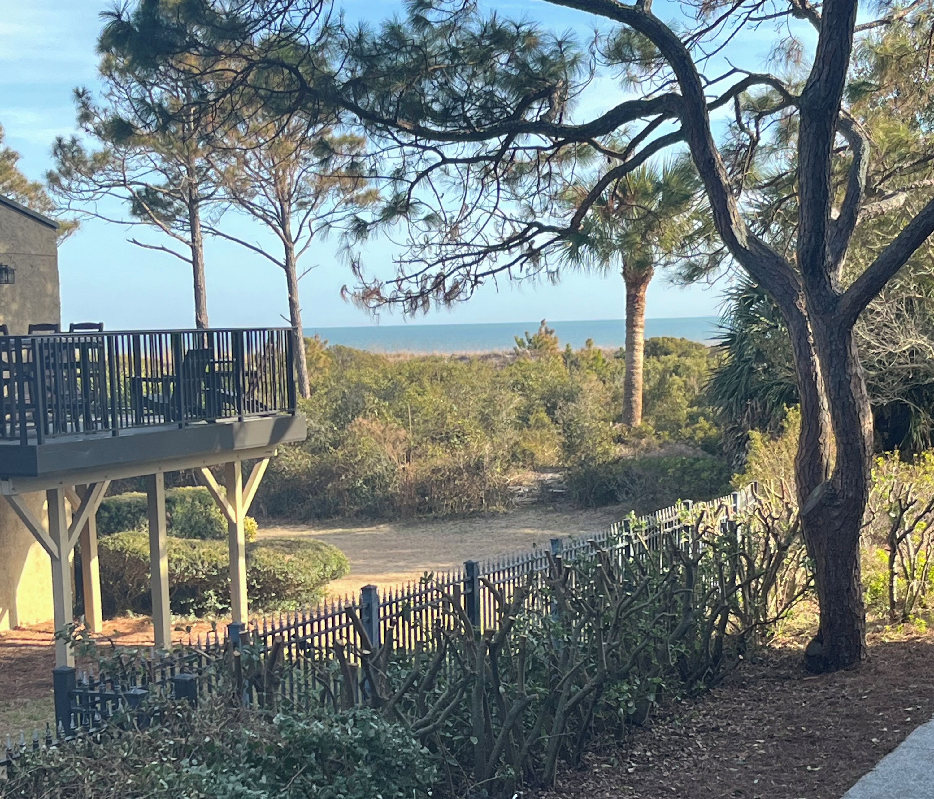 A coastal property with a balcony overlooking the sea, surrounded by dense vegetation and a fenced garden.