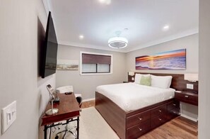 Une chambre moderne avec un grand lit, un bureau, une chaise, un téléviseur à écran plat fixé au mur et une fenêtre avec des stores.