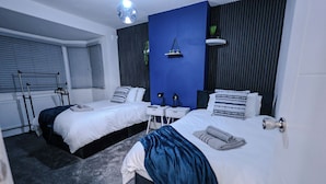 A modern hotel room with two beds, a blue accent wall, a small bedside table with a lamp, and a radiator. - Sleeps17 Bliss 7-bedroom Luxury Escape Birmingham (Birmingham)