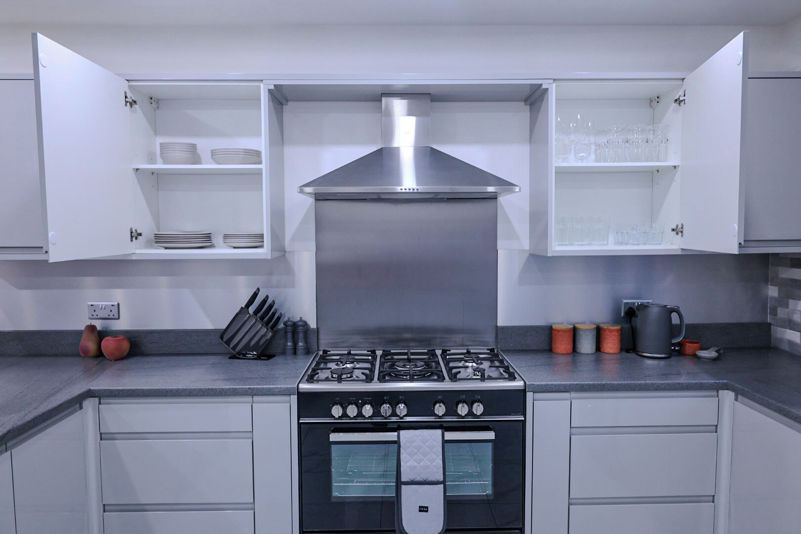 Uma cozinha moderna com armários brancos, exaustor de aço inoxidável, fogão a gás e forno embutido.