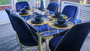A dining table set with blue and gold plates, bowls, and cutlery, surrounded by matching chairs. - Sleeps17 Bliss 7-bedroom Luxury Escape Birmingham (Birmingham)