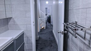 A narrow hallway with a white bathtub on the left, a handrail on the right, and a staircase in the background. - Sleeps17 Bliss 7-bedroom Luxury Escape Birmingham (Birmingham)