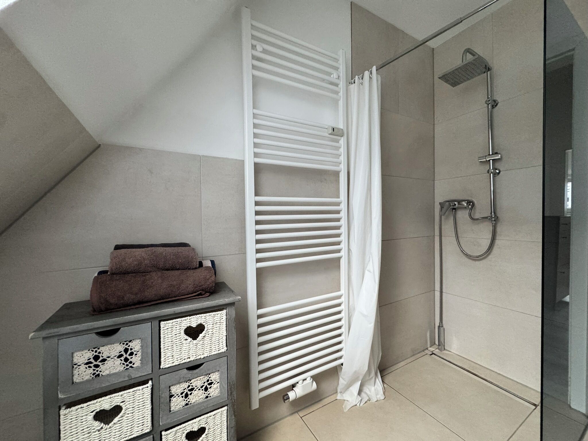Un baño moderno con ducha, un perchero y un mueble de almacenamiento con cajones decorativos.