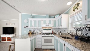 A compact kitchen with white and light blue cabinets, a granite countertop, a stove, and a sink.