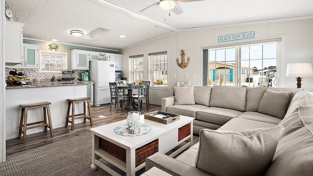 A spacious living room with a large beige sofa, a coffee table, and a dining area with a kitchen in the background.