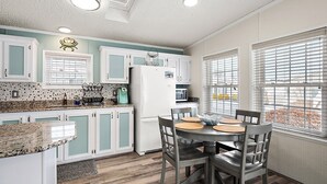 A compact kitchen with teal cabinets, a white refrigerator, and a dining area with four chairs.
