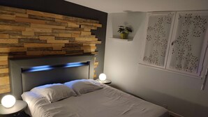 Un dormitorio moderno con cabecera de madera, cama con ropa de cama blanca, dos lámparas de noche y una ventana con cortinas decorativas.