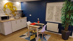 Cocina compacta con armarios blancos, microondas y cafetera. Cuenta con un comedor con mesa, sillas y una planta en maceta.