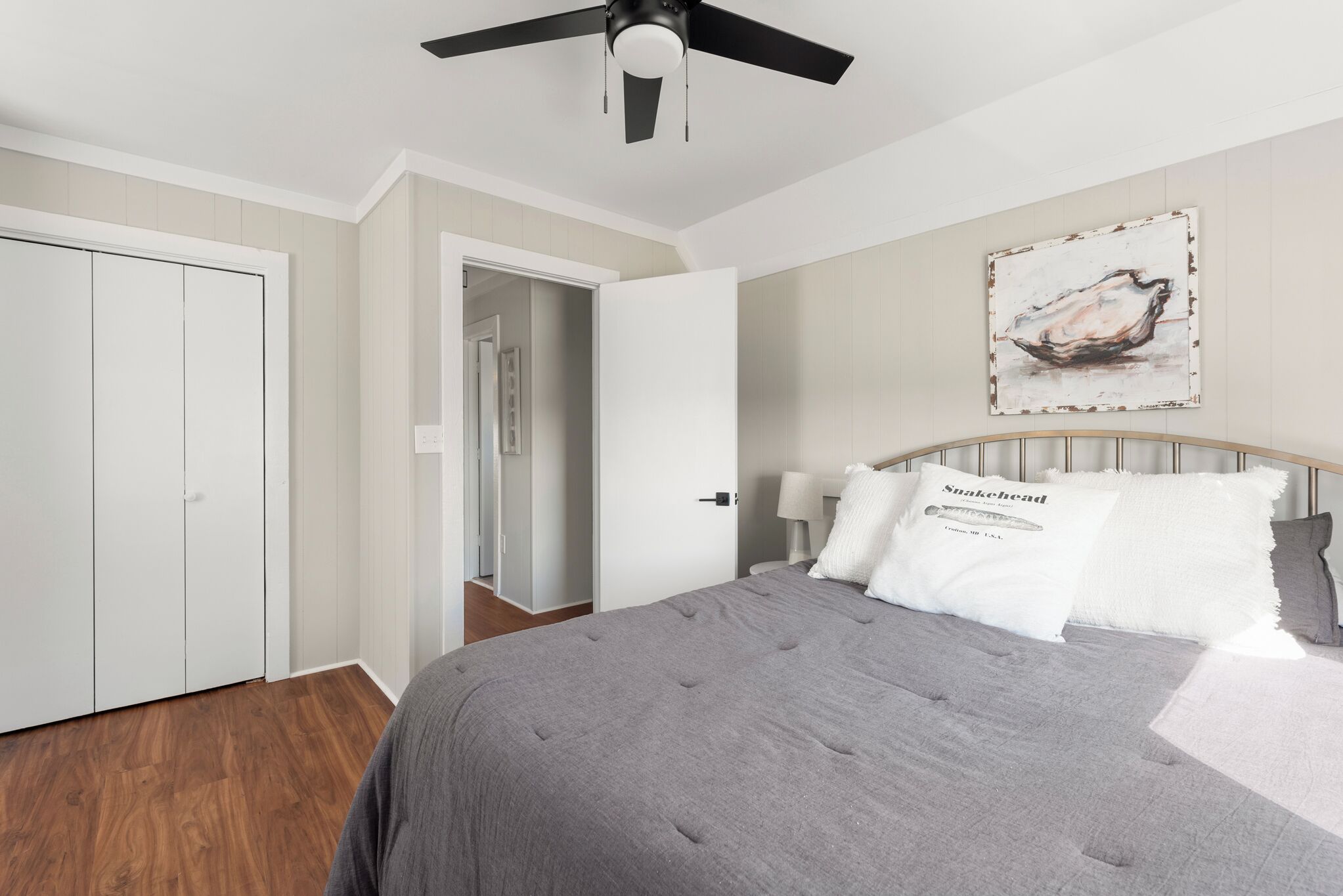 A bedroom with a bed, a ceiling fan, a door, and a wall with a painting.