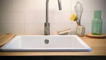 A kitchen with a white sink, a stainless steel faucet, a wooden countertop, a whisk, and a green bottle.
