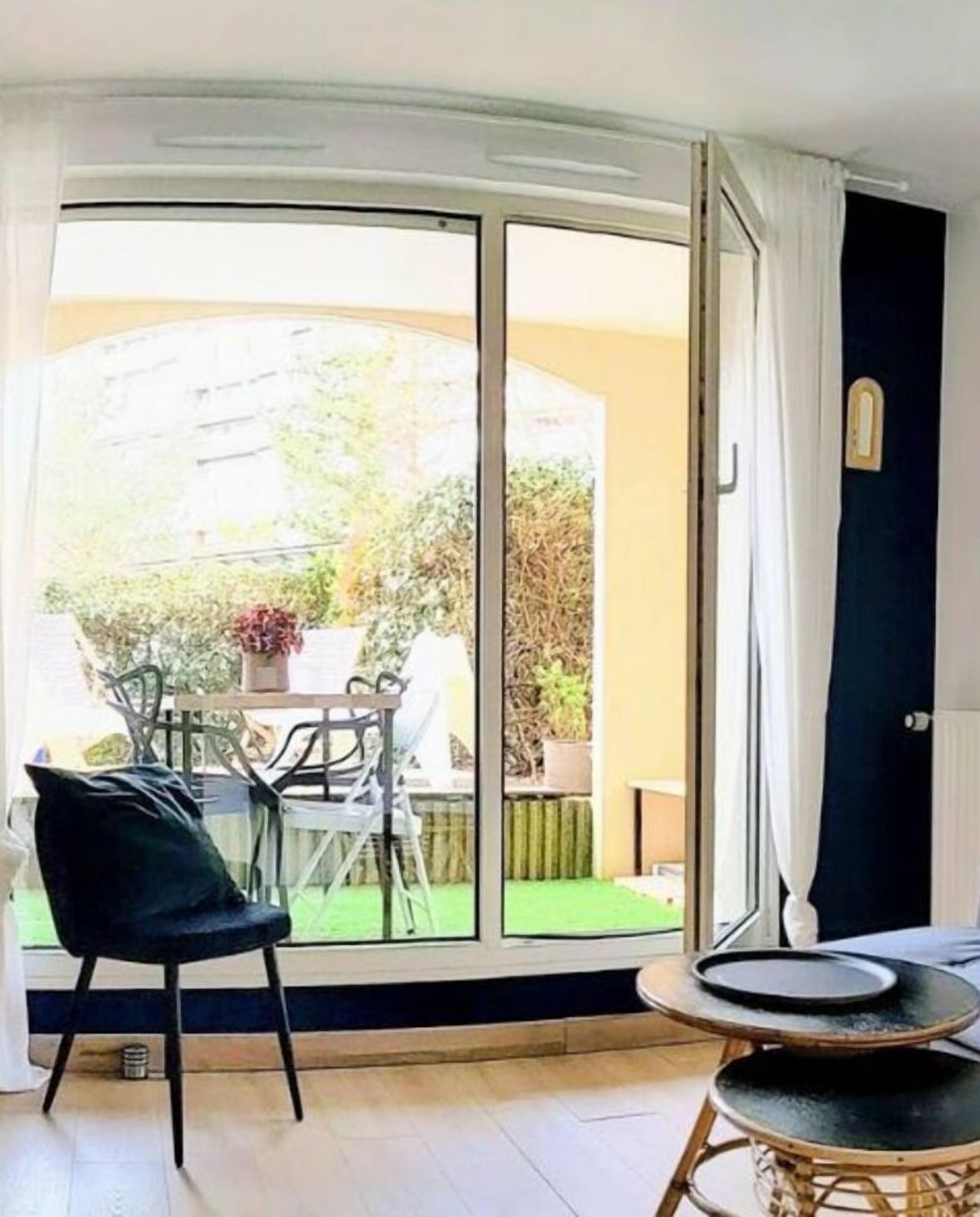 A room with a sliding glass door leading to a garden, a black chair, and a small round table.
