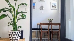 A room with a large potted plant, a wooden dining table with two chairs, and a wall decorated with framed pictures and geometric mirrors. - Charming with Garden | Near train station (Rennes)