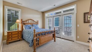 Ein Schlafzimmer mit einem hölzernen Bett, einem Nachttisch, einer Kommode und einem großen Fenster mit Jalousien.
