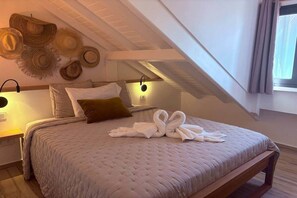 Quarto com teto inclinado, cama com colchão acolchoado, travesseiro marrom e arranjo de toalhas.