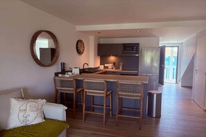 Cozinha moderna com ilha central, banquetas e área de jantar com sofá e um espelho decorativo.