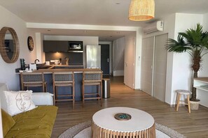 Uma sala de estar moderna com sofá, mesa de centro redonda e área de cozinha com micro-ondas, geladeira e banquetas.