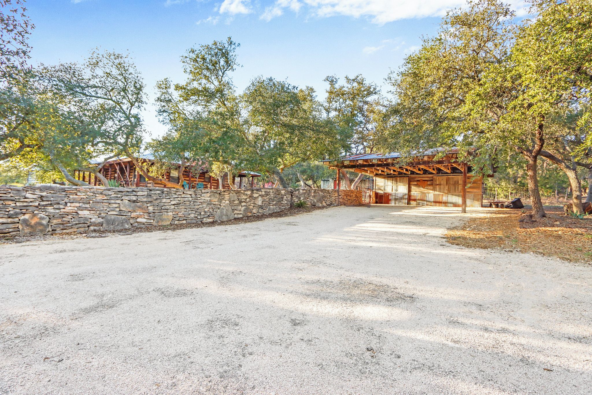 Ein rustikales Blockhaus mit Steinmauern und Holzbalkon, umgeben von Bäumen und einem Kiesweg.