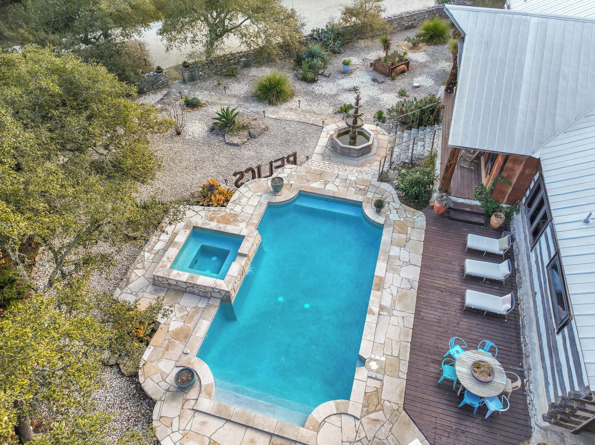 A swimming pool with a hot tub, surrounded by a stone deck and various plants.