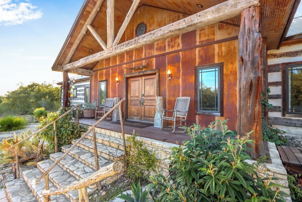 A rustic cabin with a wooden exterior, stone steps, and a porch with two chairs.