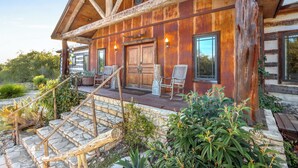 Un rustico chalet con facciata in legno, gradini in pietra e un portico con due sedie.