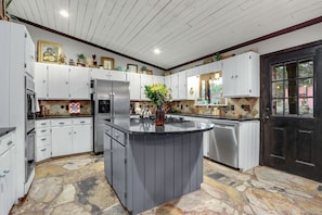 A kitchen with white cabinets, a central island, a black door, and a stone-patterned floor.