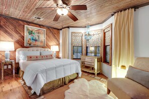 Een slaapkamer met een houten plafond, een bed met witte beddengoed, een nachtkastje, een dressoir en een stoel.