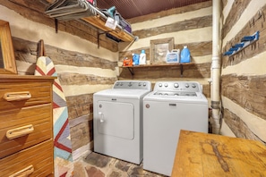 A laundry room with two washing machines, a wooden dresser, and shelves with cleaning supplies.