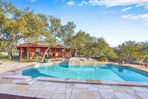 Una piscina con piastrelle in pietra, una casetta di legno e alberi circostanti.