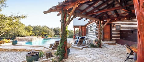 A rustic cabin with a stone patio, outdoor seating, and a swimming pool.