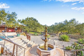 A rustic outdoor area with a stone staircase leading to a wooden deck, a small pool, and a decorative fountain surrounded by desert plants.