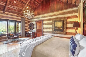 Une chambre à coucher rustique avec un grand lit, des murs en bois, un lustre et une vue sur l’extérieur.