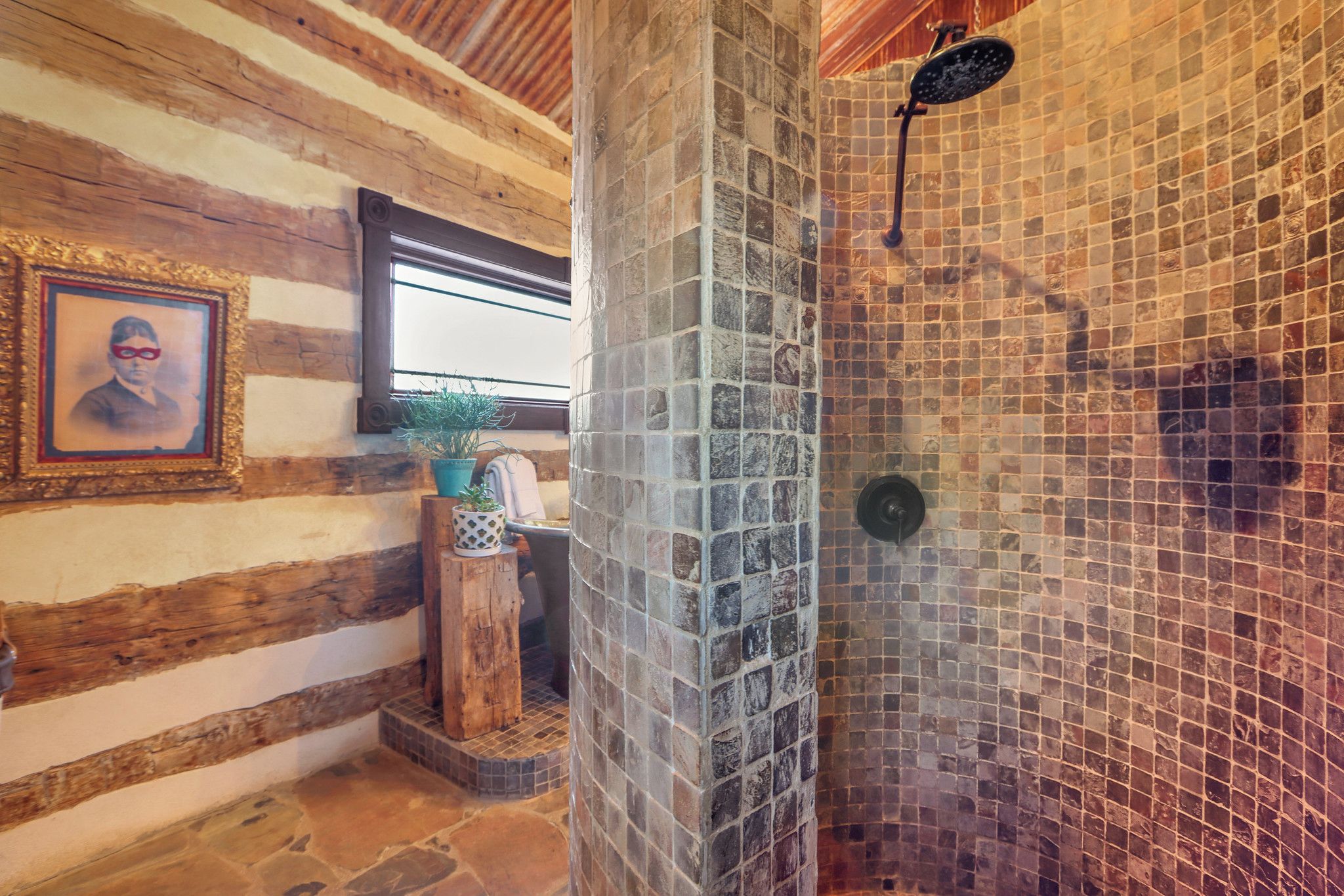 A rustic bathroom with a stone shower, wooden beams, and a framed picture on the wall.