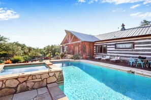A wooden cabin with a swimming pool, outdoor seating, and a stone wall.
