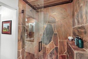 A stone shower enclosure with a glass door, a towel rack, and toiletries on a shelf.
