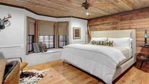 A bedroom with a wooden ceiling, a bed with white bedding, a cowhide rug, and a deer head decoration. - Luxury Ranch w/ Pool, Hot Tub, Chef's Kitchen + Close to Wineries (Wimberley)