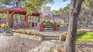 Un patio al aire libre rústico con una chimenea de piedra, mesas y sillas de madera.