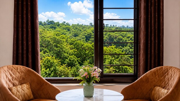 A room with two chairs, a table, and a window with a view of a forest. - Opal Villa by JMD Group (New Delhi)