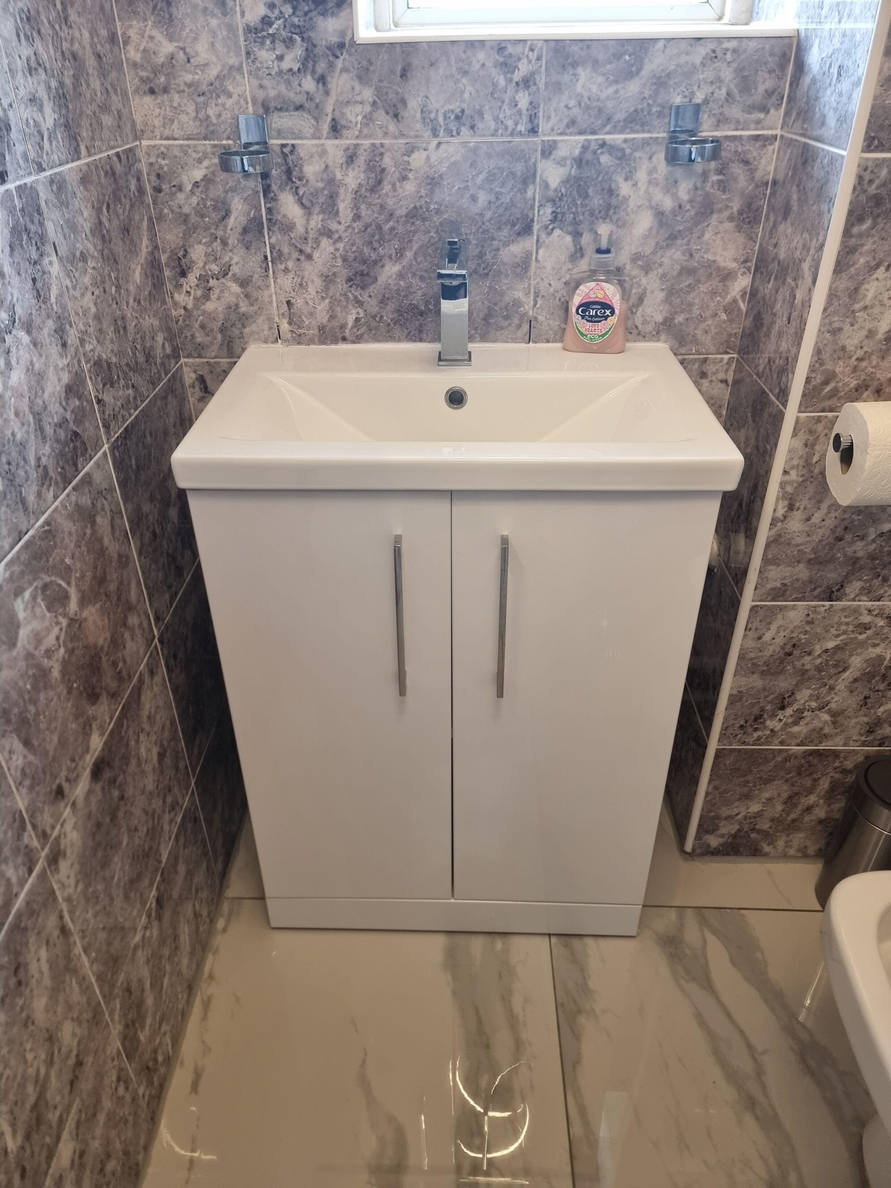 Un baño con lavamanos blanco, azulejos de mármol y un inodoro.
