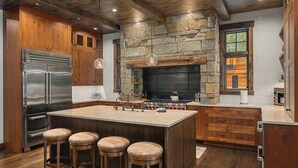 Una cocina con una isla central, armarios de madera, una chimenea de piedra y un refrigerador de acero inoxidable.