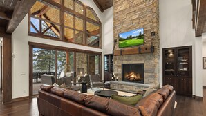 Un salón amplio con chimenea de piedra, sofá de cuero y un televisor grande montado en la pared.