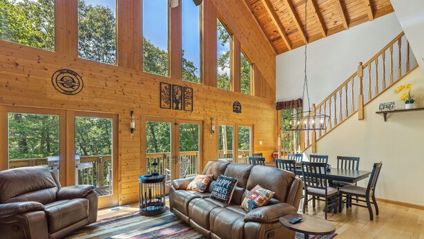 A spacious living area with a leather sofa, dining table, and chairs, large windows, and a wooden ceiling.