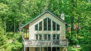 A two-story cabin with a balcony, surrounded by dense forest.