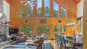 A spacious living area with a fireplace, leather seating, a dining table, and large windows offering views of the outdoors.