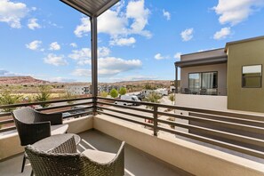 A balcony with wicker chairs and a view of a modern building and distant hills.