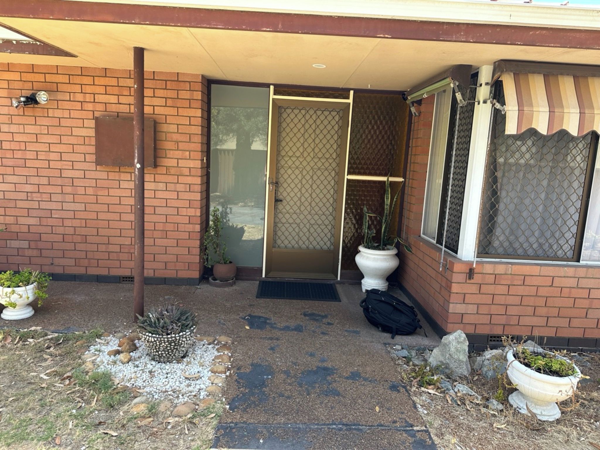A brick building with a sliding glass door entrance, a potted plant, and a small outdoor area with gravel and rocks.