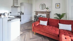 Eine moderne Küche mit weißen Schränken, ein Essbereich mit einem roten Sofa und ein Kamin.